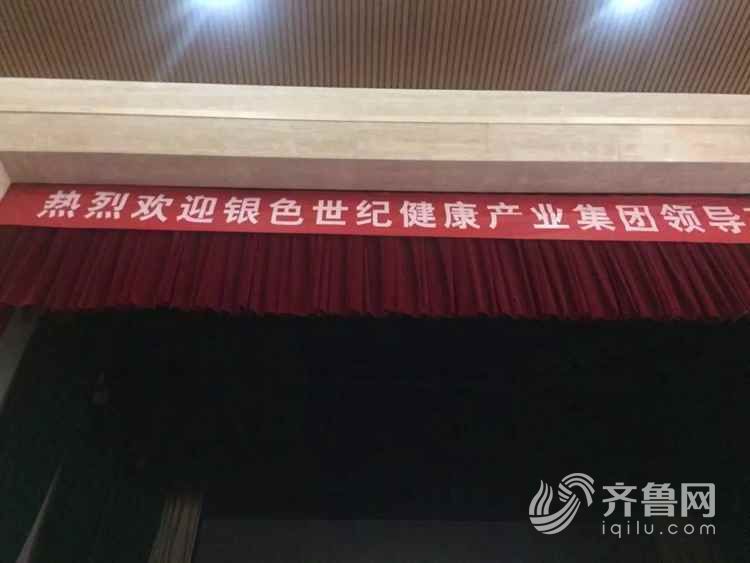 讲台上悬挂着"欢迎银色世纪健康产业集团领导莅临济南"的红色横幅
